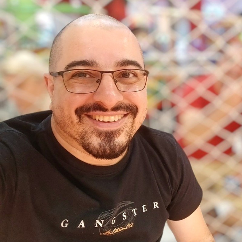Foto do Edilberto usando óculos, uma camisa preta e com fundo desfocado